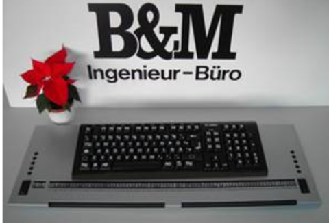Black keyboard with white keys on a gray desk against a white wall with the company logo painted in black.
