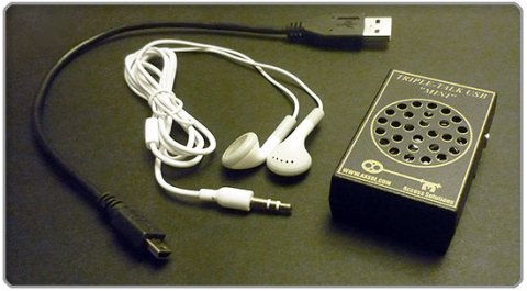 A medium-sized black device with a built-in speaker, roughly the size of a smartphone. Next to it are white earbuds and a USB cord.