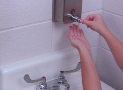 An image of someone using a soap dispenser to wash their hands at a sink.