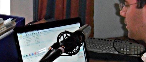 A man speaking into a microphone and looking at a laptop.