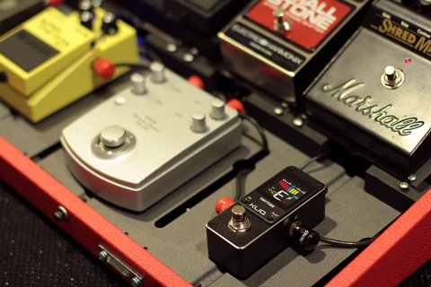 Image of several guitar and bass pedals next to a small, rectangular, and black device.
