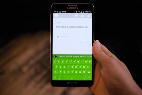 Picture of a hand holding a smartphone displaying the app, with a light green keyboard on the bottom and a text window on the top.