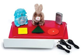 Rectangular white device with red surface and three toys on top next to three geometric shapes. Three black cables are on the lower right.