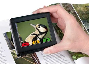 Picture of a hand holding a small video screen, which is being held over a book and shows a magnified image of a bird.