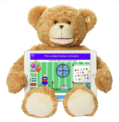 Sammy the Bear is plush brown with small black eyes and a white muzzle and footpads. He is sitting with an iPad in his lap which has a screen picturing a room with green wallpaper, a round window, balloons by shelves, a whiteboard with the alphabet in different colors and a robot.