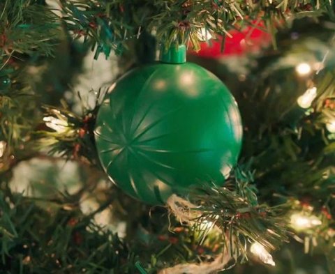 A round green Christmas tree ornament hanging from a branch.