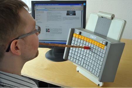 The keyboard attached to a stand being used with a mouth stick. 