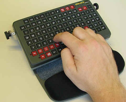 Small rectangular keyboard with hand on palm rest pushing the keys.