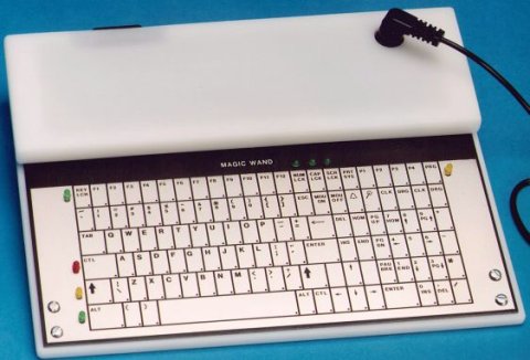 A medium-sized keyboard with full QWERTY layout and a built in mouse. The keyboard is off-white, witb a long bar that runs the length of they keyboard at the top with a black cord connecting to it.