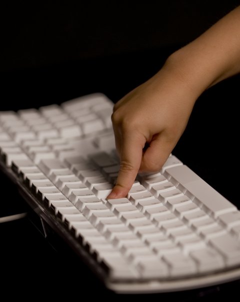 A hand pressing on a keyboard using only one finger.