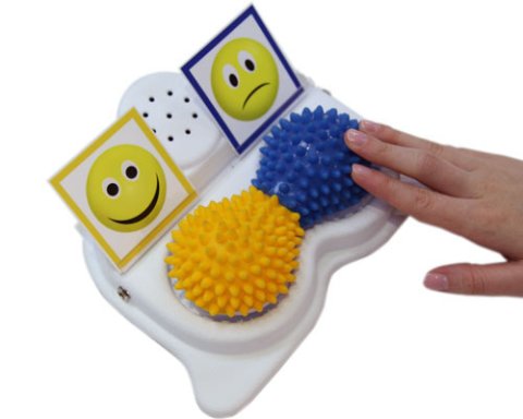 Yellow and blue texture pads in front of smiley and frowny face icons mounted on white base with speaker in center.