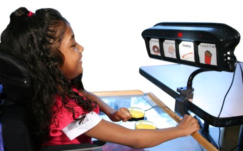 A child facing scanner on an arm secured to a table. The scanner has four images displayed and a wire extending from the bottom right edge.