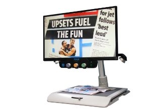 Large-screen monitor with a platform base underneath for placing materials on and magnifying them. The monitor's front panel has three small, round knobs. The monitor screen is displaying a magazine's front page.