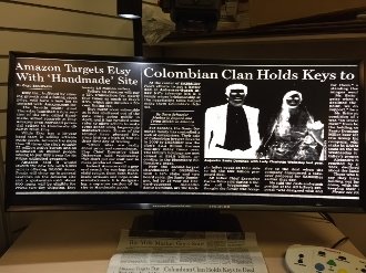 Large curved flat screen monitor, displaying a magnified newspaper page in high contrast white-on-black.