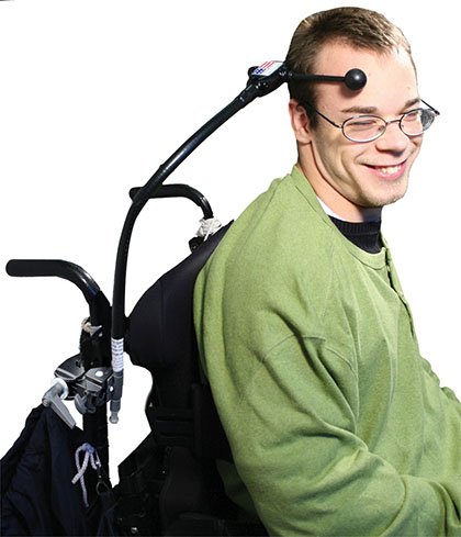 Person in wheelchair with switch attached to chair and head.