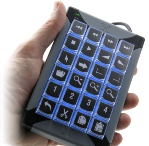 A hand holding a small keyboard device the size and shape of a numeric keypad on a standard keyboard. There are twenty keys, which are labeled with various alphanumeric symbols. The device base is black, and the keys are black with blue backlighting.