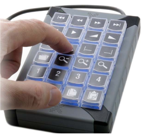 A user presses a key on a small keyboard device the size and shape of a numeric keypad on a standard keyboard. There are twenty keys, which are labeled with various alphanumeric symbols. The device base is black, and the keys are black with blue backlighting.
