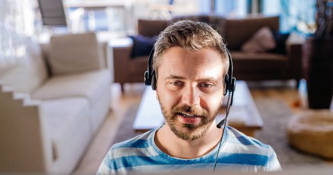 The torso view of a man facing forward wearing a headset and a living room behind him.