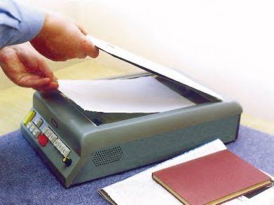 A medium-sized grey device resembling a scanner. A user is lifting the top and placing a sheet of paper on the scanning bed.