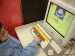Image of a user pressing a key on the keyboard, while the computer monitor displays a pale yellow screen with an of a hat and the letters "HA."