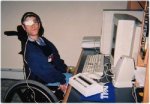 A man with one eye closed sitting on a wheelchair infront of a computer using VisionKey
