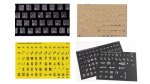 Various models of Braille computer keyboard stickers. They resemble sticker sheets with individual stickers corresponding to each letter on a keyboard. Two models feature only Braille on each key; the other two feature high-contrast letters printed in addition to Braille characters. Two models are black; one is off-white; and the fourth is yellow.