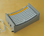 A corded, elevated keyboard with keys arranged within a tight, rectangular area along a downwardly curved surface. They keyboard is grey in color.