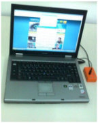 A silver, open laptop next to a bright orange rectangular switch connected via a black cord.