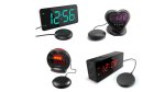 Various models of extra loud alarm clock with bed shaker. Two of them resemble a standard rectangular alarm clock, but with a small, black, and round component (resembles a "hockey puck") attached to it via cord. Two of the alarm clocks are smaller; one is a circular clock with a flat base for standing upright. The other is small and heart-shaped. One model has teal clock numbers; two have red; and a fourth has purple clock numbers.