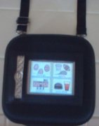 Small black square electronic device attached to a neck strap with a display showing a grid of four images.