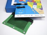 Shown is what's included: large printout of United States map, folded atop the box, with states in different colors, a green plastic pouch on the lower left and a special pen and cord sitting on the map.