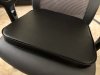Closeup of the seat of a black desk chair with a black foam cushion on it.